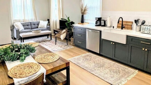 A modern kitchen with dark cabinets, a wooden dining table, and a living area with a sofa and TV. - Serenity by the Sea (Samoa)