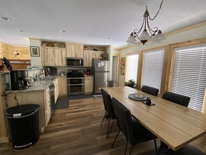 Ett modernt kök med träskåp, vitvaror i rostfritt stål och en matplats med ett träbord och stolar.