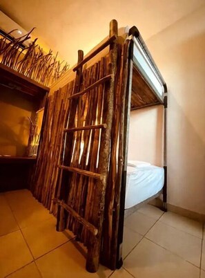 Un letto a castello con una scaletta, pannelli di legno al muro e uno scaffale con piante essiccate.