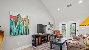 A spacious living room with a large painting, a television, a wooden coffee table, a leather armchair, and a sofa. - Lone Star Cabin No. 9 (Fredericksburg)