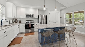 A modern kitchen with white cabinets, stainless steel appliances, a granite countertop, and a large island with bar stools. - Lone Star Cabin No. 9 (Fredericksburg)