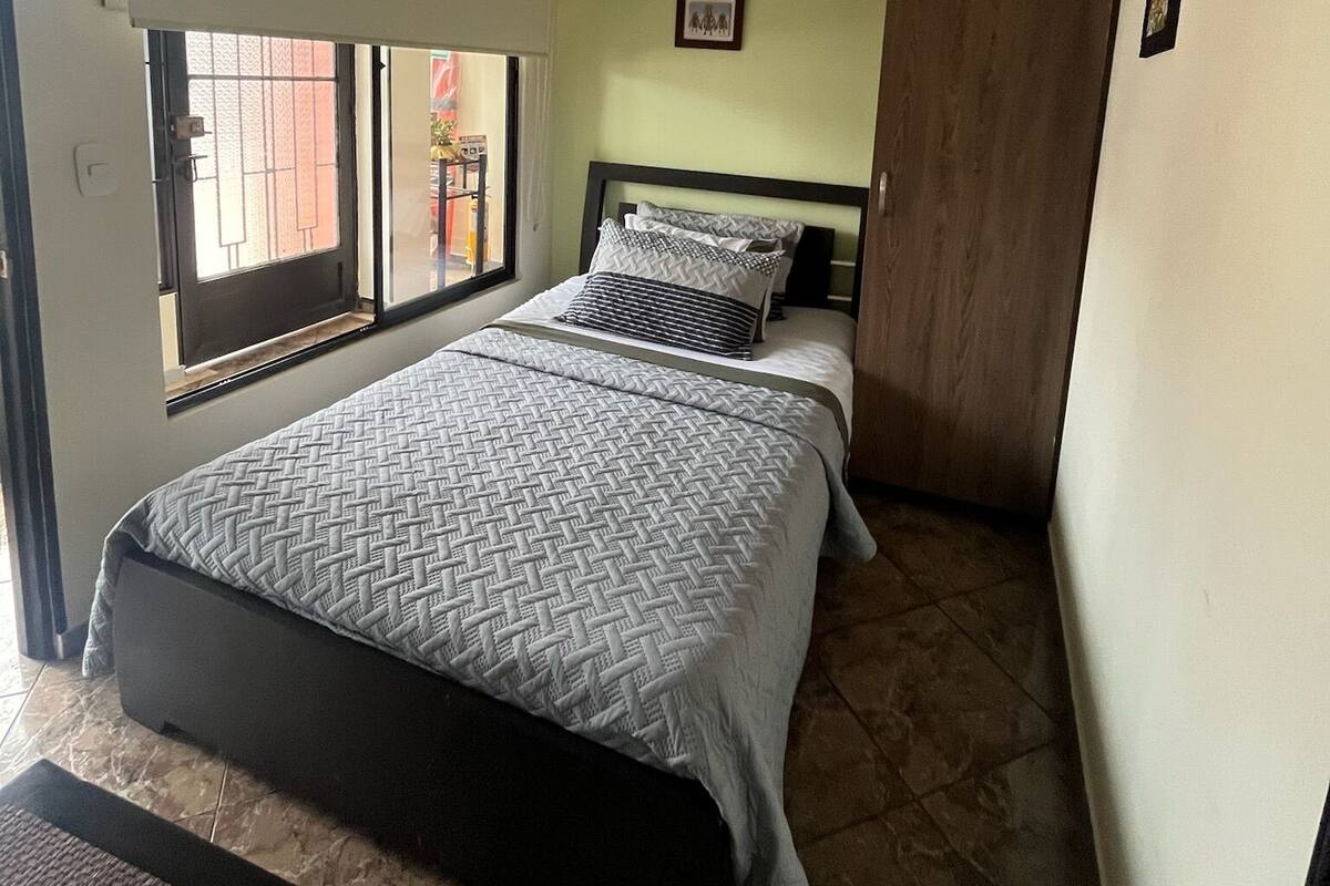 Een slaapkamer met een bed, een raam, een deur en een aan de muur hangend schilderij.