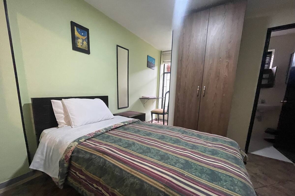Een slaapkamer met een bed, een garderobe, een stoel en een klein tafeltje.