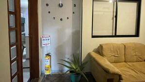 Une pièce avec un canapé beige, une horloge au mur, une plante en pot et un extincteur.