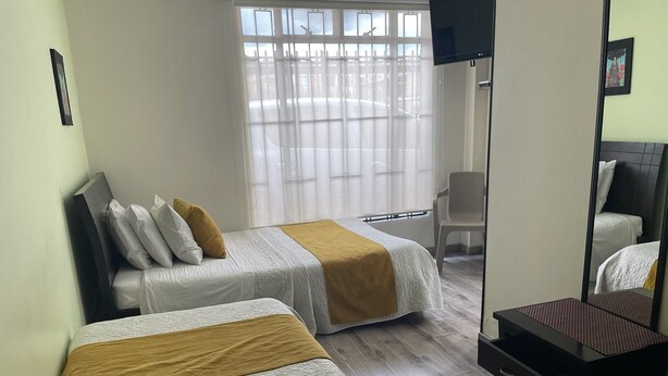 Une chambre d’hôtel avec deux lits, un bureau, une chaise, une télévision et une fenêtre avec des stores.