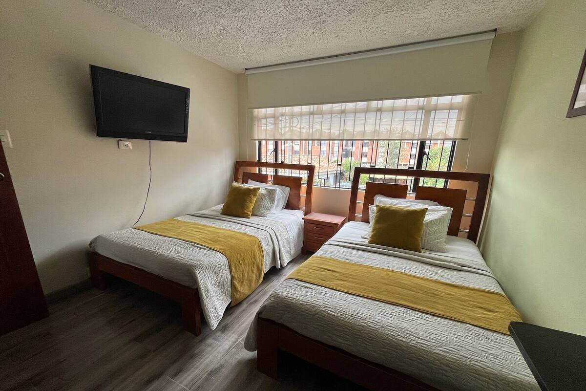 Een hotelkamer met twee bedden, een aan de muur bevestigde televisie en een raam met jaloezieën.