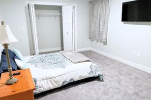 A bedroom with a bed, a nightstand, a lamp, a closet, and a TV on the wall. - Whispering Pines: Nearby Kingston Lake | Monthly (Kingston)