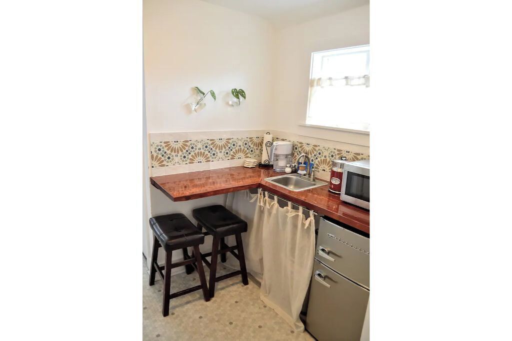 Cocina compacta con encimera de madera, dos taburetes, un lavabo, microondas y refrigerador.