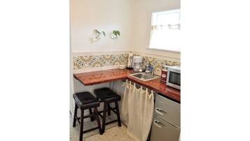 Cocina compacta con encimera de madera, dos taburetes, un lavabo, microondas y refrigerador.