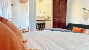 Une chambre à coucher avec un lit, une porte en bois et un coin repas visible à travers une porte ouverte.