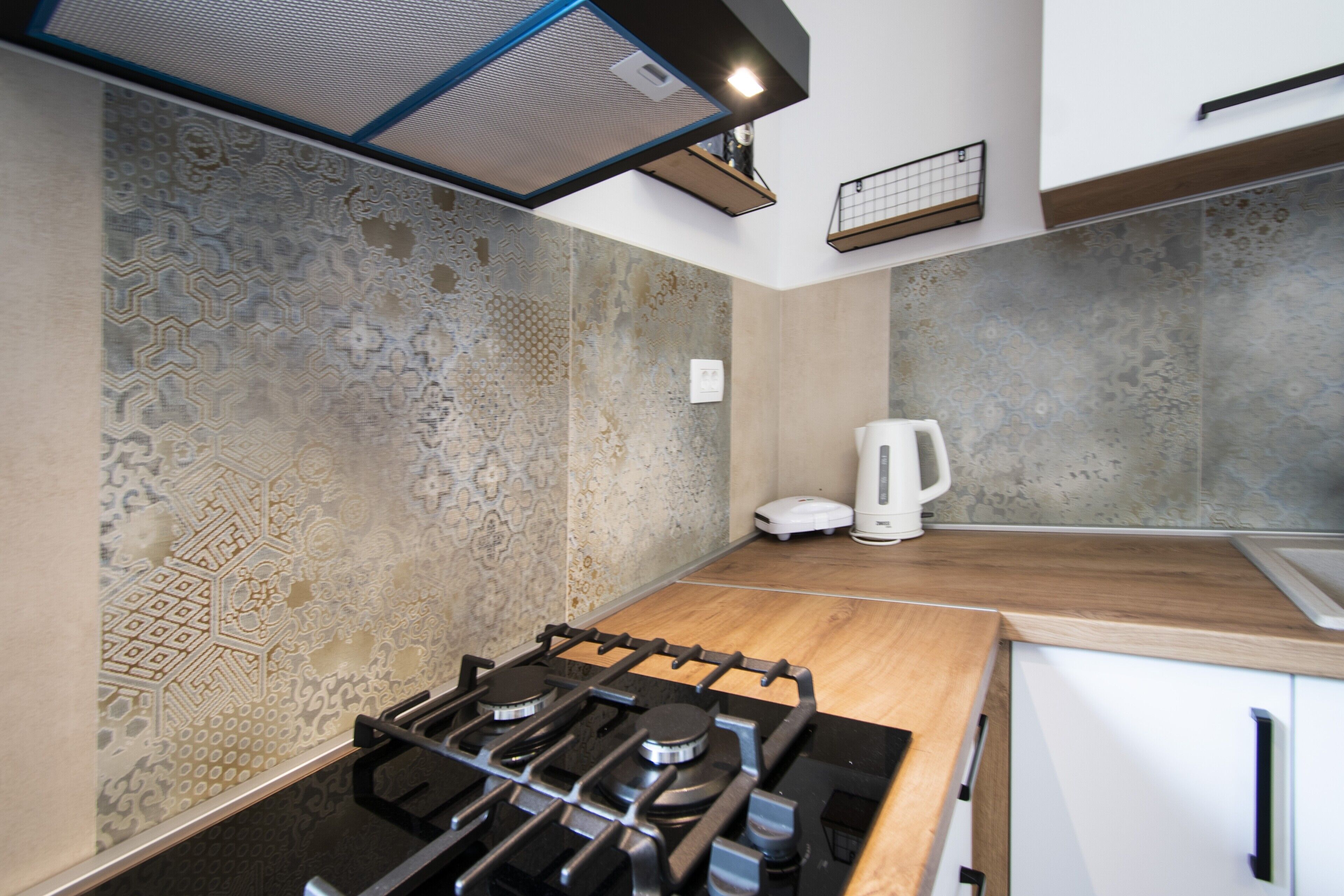 A modern kitchen with a gas stove, white cabinets, and patterned backsplash.
