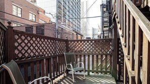 Un terrazzo in legno con una recinzione a graticcio, due sedie e vista su alti edifici.