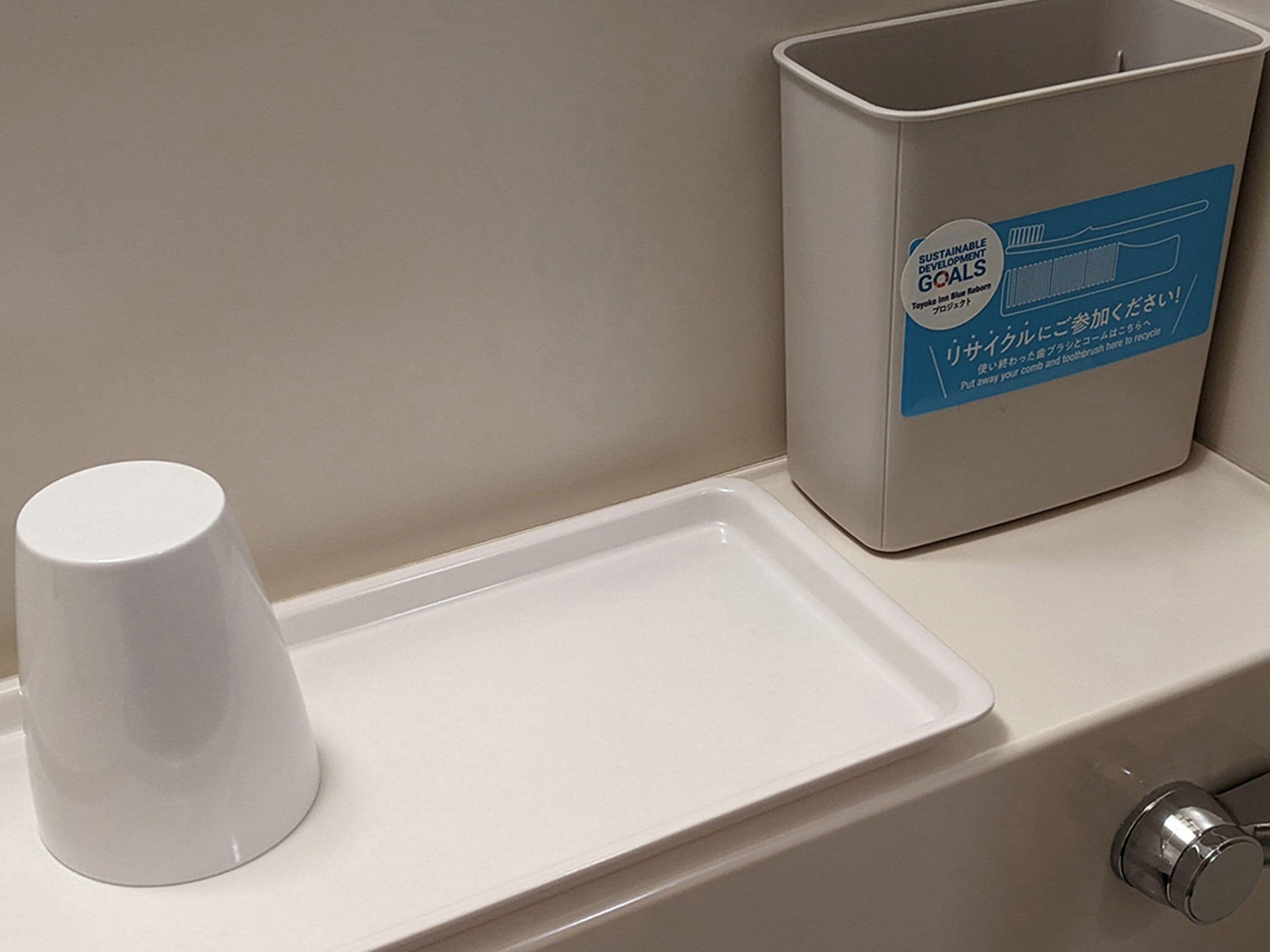 A bathroom sink with a white cup holder and a trash bin labeled 'Sustainable Developments Goal Blue Bottle'.