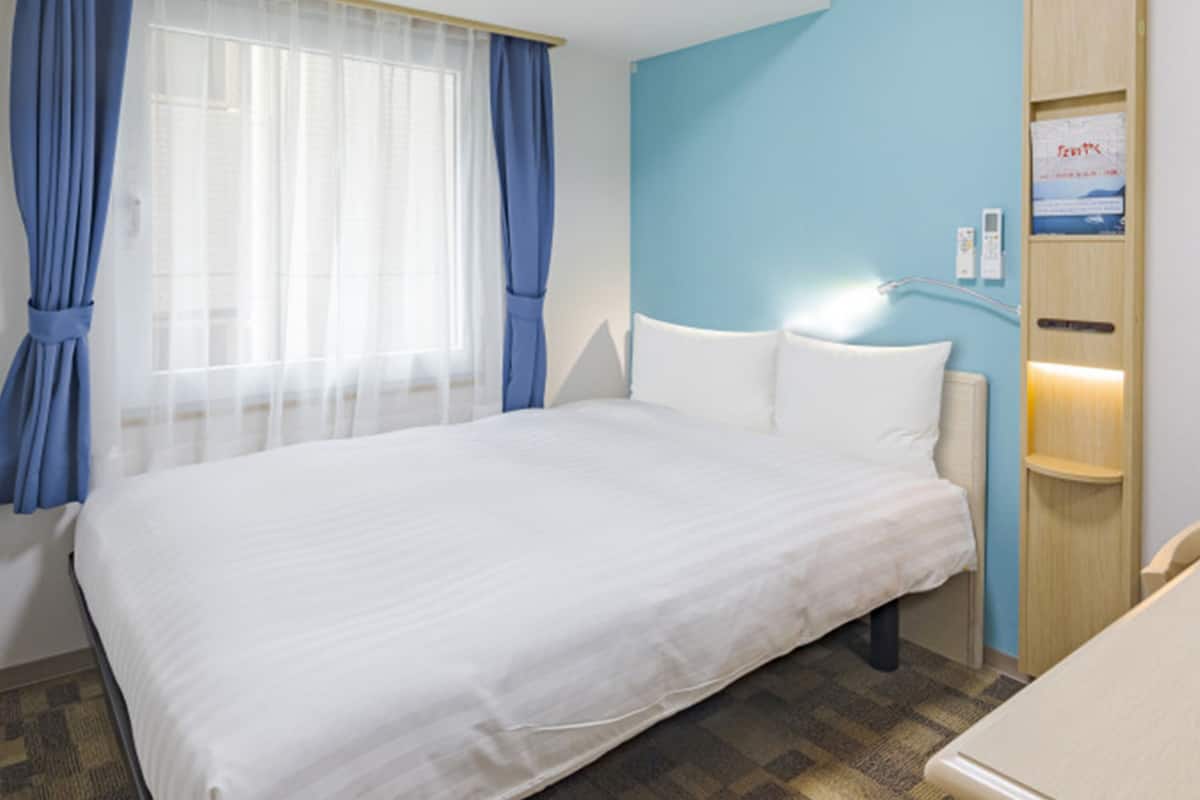 Ein Hotelzimmer mit einem großen Bett, einem Nachttisch, einer Wandlampe und einem Fenster mit Vorhängen.