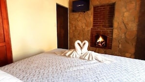 Un dormitorio con una cama grande, pared de piedra, chimenea y televisión.