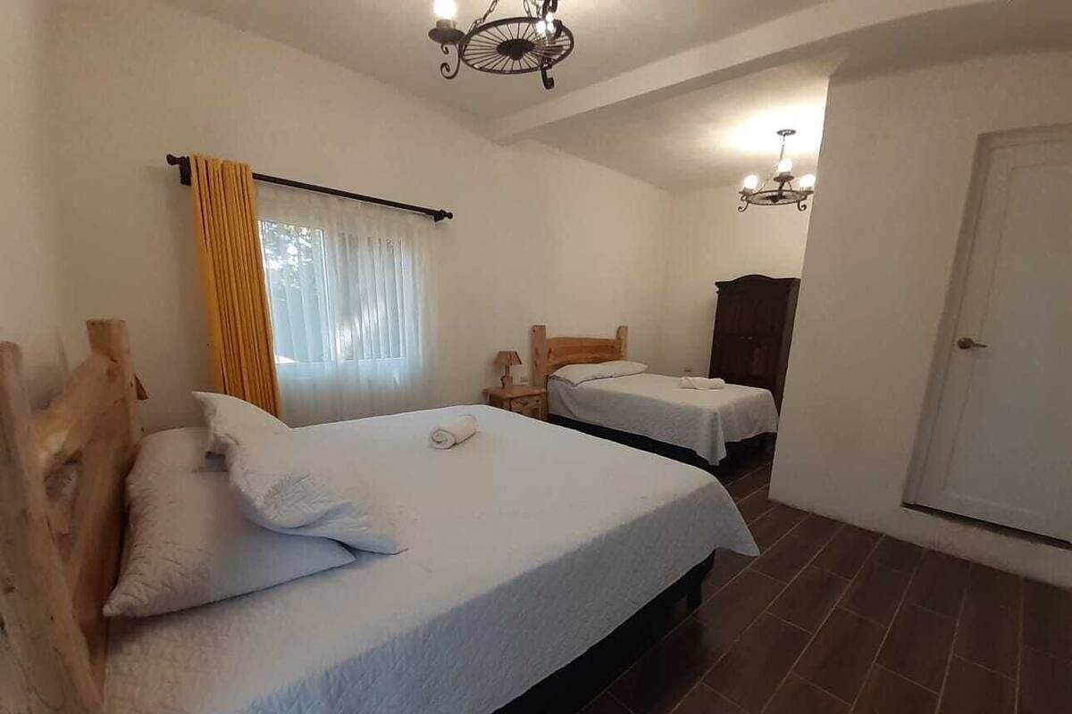 A bedroom with two beds, a wooden headboard, a nightstand, a wardrobe, and a chandelier.