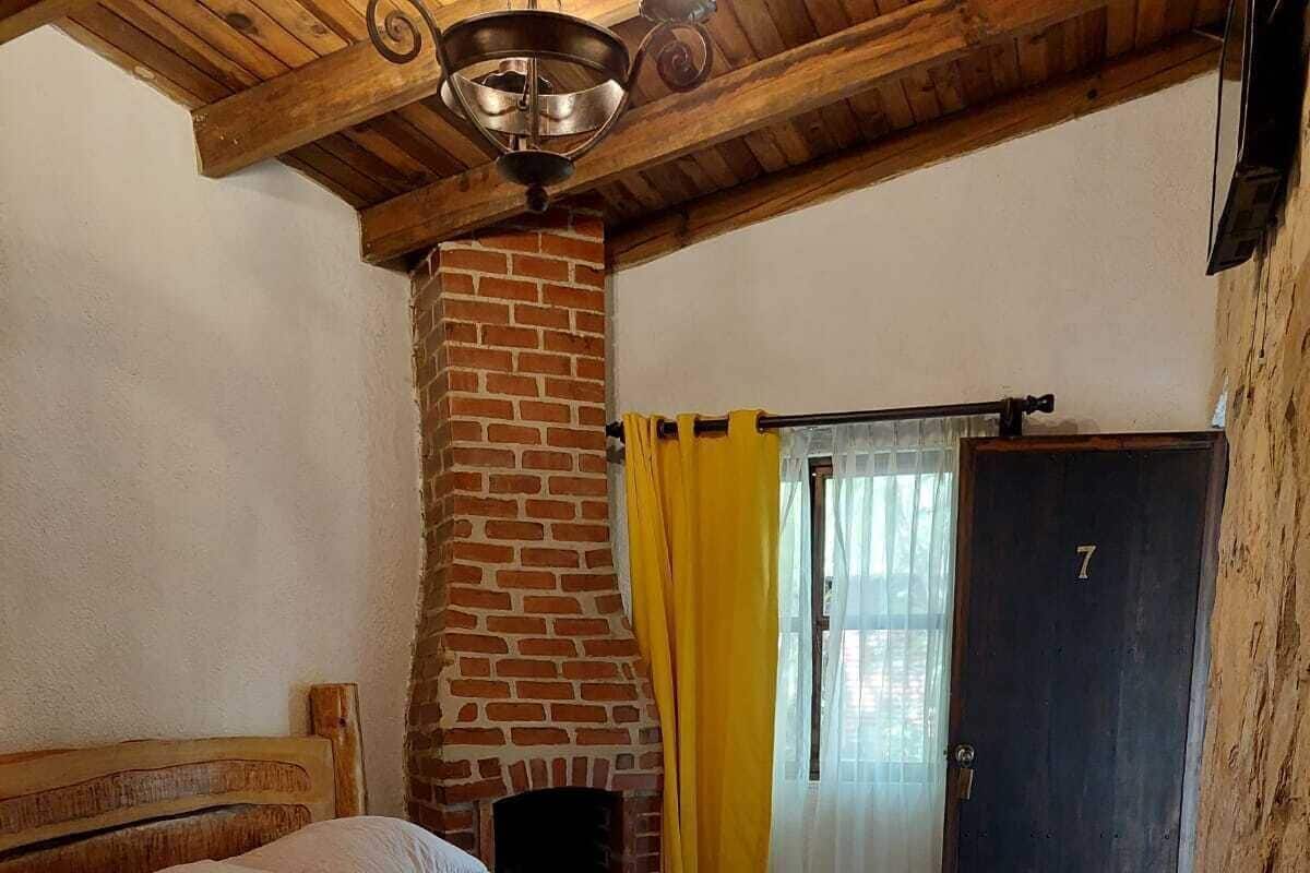 A bedroom with a brick fireplace, a bed with a headboard, a wooden ceiling, and a door marked with the number 7.