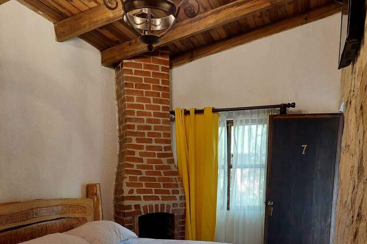 A bedroom with a brick fireplace, a wooden ceiling, and a bed with a white quilt.