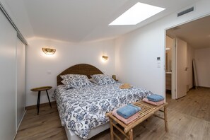 Une chambre à coucher avec un lit, des tables de chevet, un banc et une lucarne.