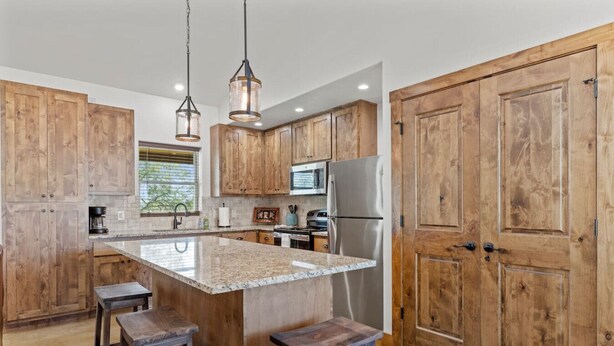 A kitchen with wooden cabinets, a central island with stools, stainless steel appliances, and pendant lighting.