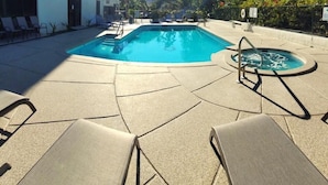 A swimming pool with lounge chairs and a hot tub, surrounded by greenery and a building with balconies. - Hawaiian Princess at Makaha Beach (Waianae)