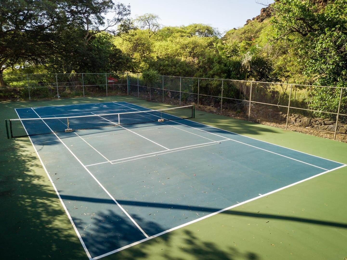An outdoor tennis court surrounded by trees and a fence.
