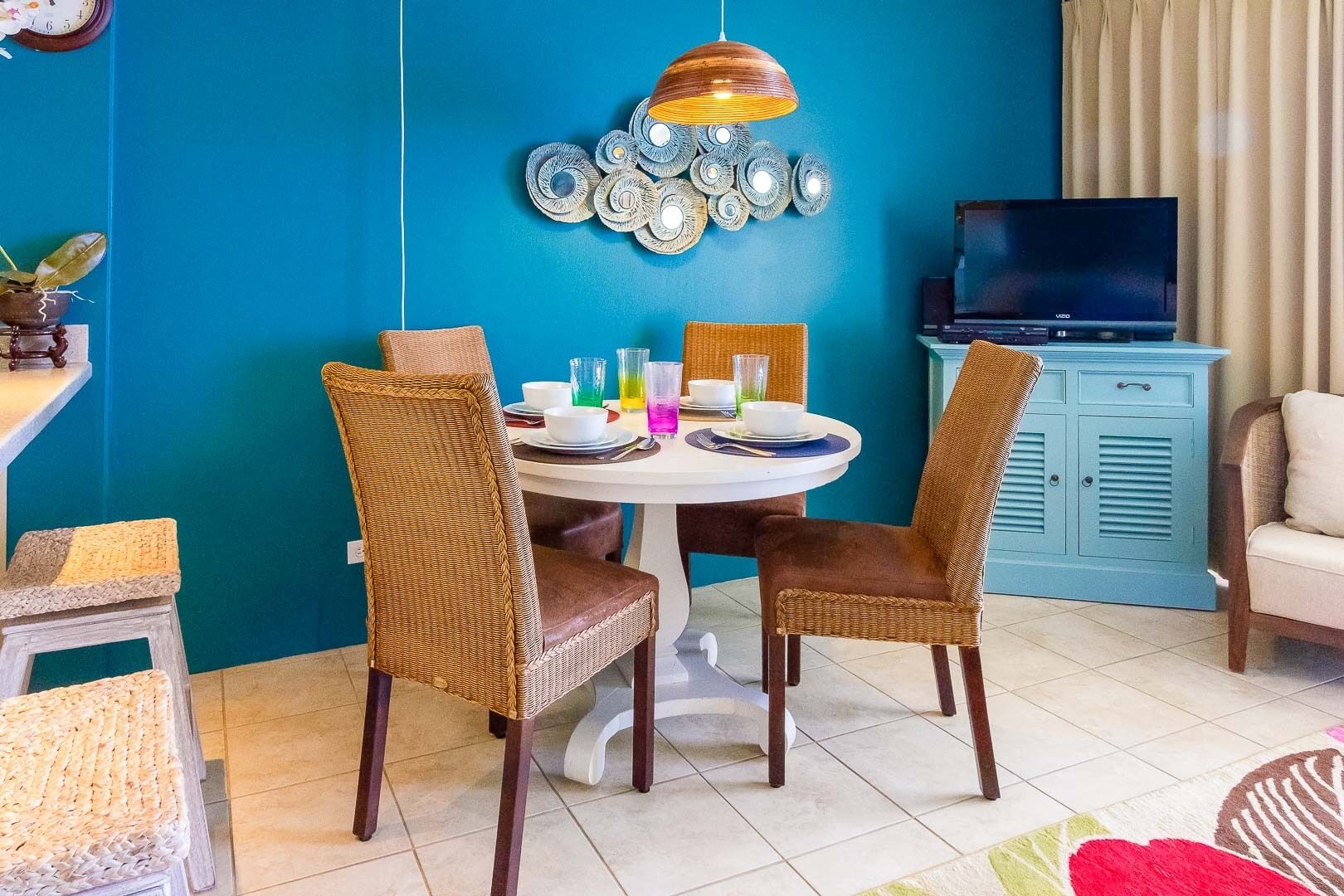 Ein Essbereich mit einem runden Tisch, Korbstühlen und einer blauen Wand mit einem dekorativen Metallkunstwerk darüber.