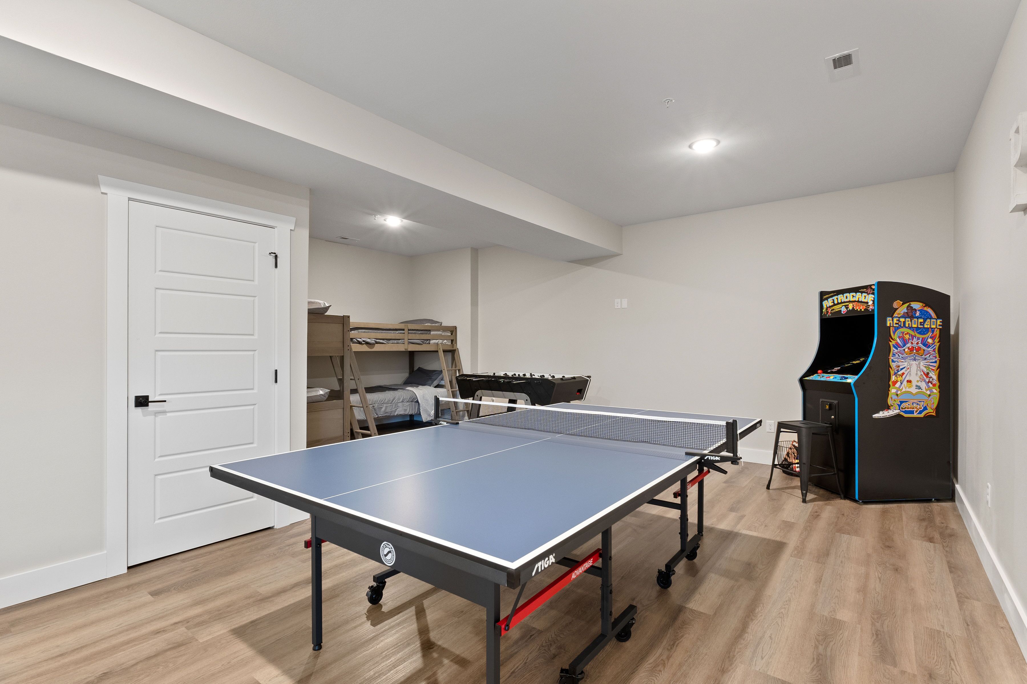 A room with a ping pong table, a bunk bed, and a retro arcade machine.