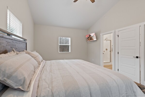 A bedroom with a bed, a window, a door, and a ceiling fan.
