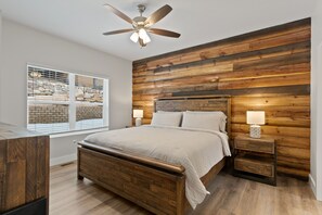 Un dormitorio con cabecera de madera, una cama con ropa de cama blanca, dos mesitas de noche con lámparas y un ventanal con persianas.