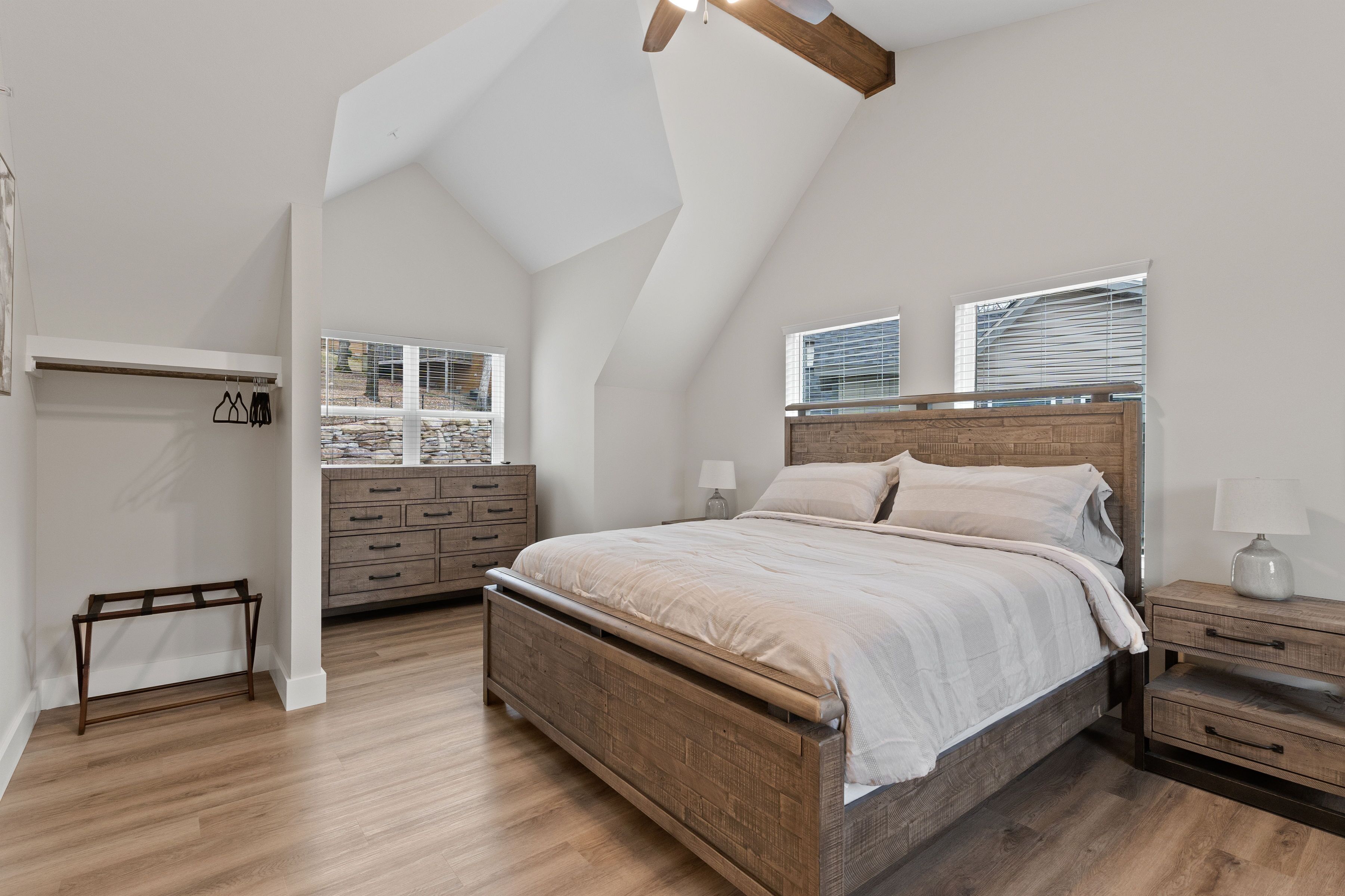 Un dormitorio con techo inclinado, una cama de madera, una mesita de noche, un aparador y una ventana con persianas.