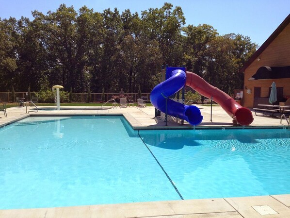 A swimming pool with a blue and red slide, surrounded by a fence and trees.