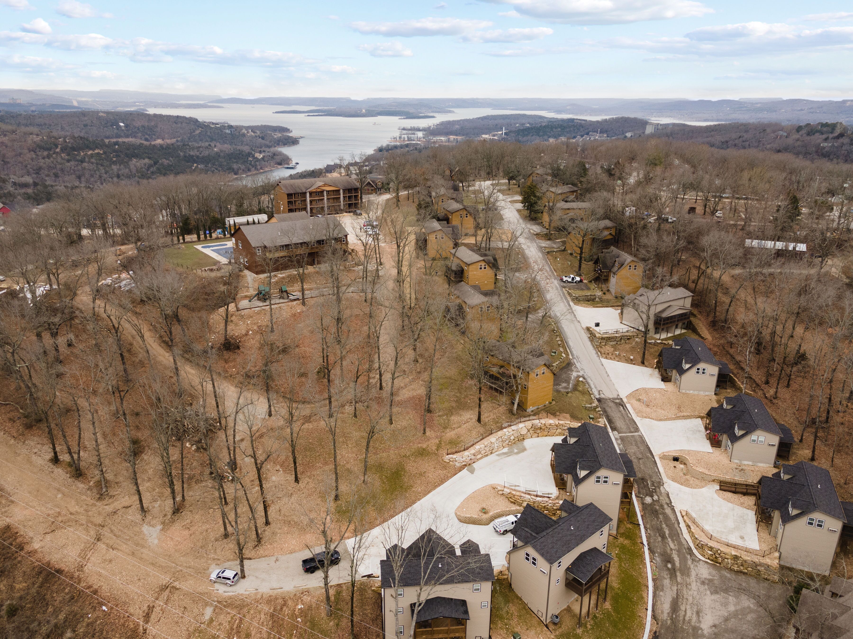 An aerial view of a residential area with houses, a road, and a body of water in the background.