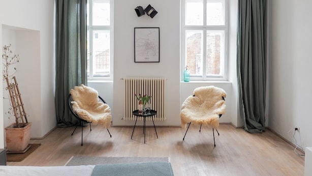 Una sala de estar moderna con dos sillones mullidos, un radiador, un mapa enmarcado y ventanas amplias con cortinas.