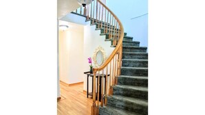 Eine Wendeltreppe mit Holzgeländern und Teppichstufen führt zu einer Empfangsebene mit einem Spiegel und einem kleinen Tisch mit einer Topfpflanze.