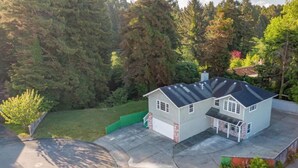 Ein zweigeschossiges Haus mit Garage, umgeben von einem gepflegten Rasen und dichten Bäumen.
