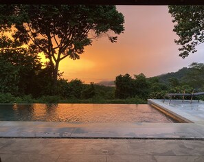 Una piscina con vista sul tramonto, immersa nel verde e alberi.