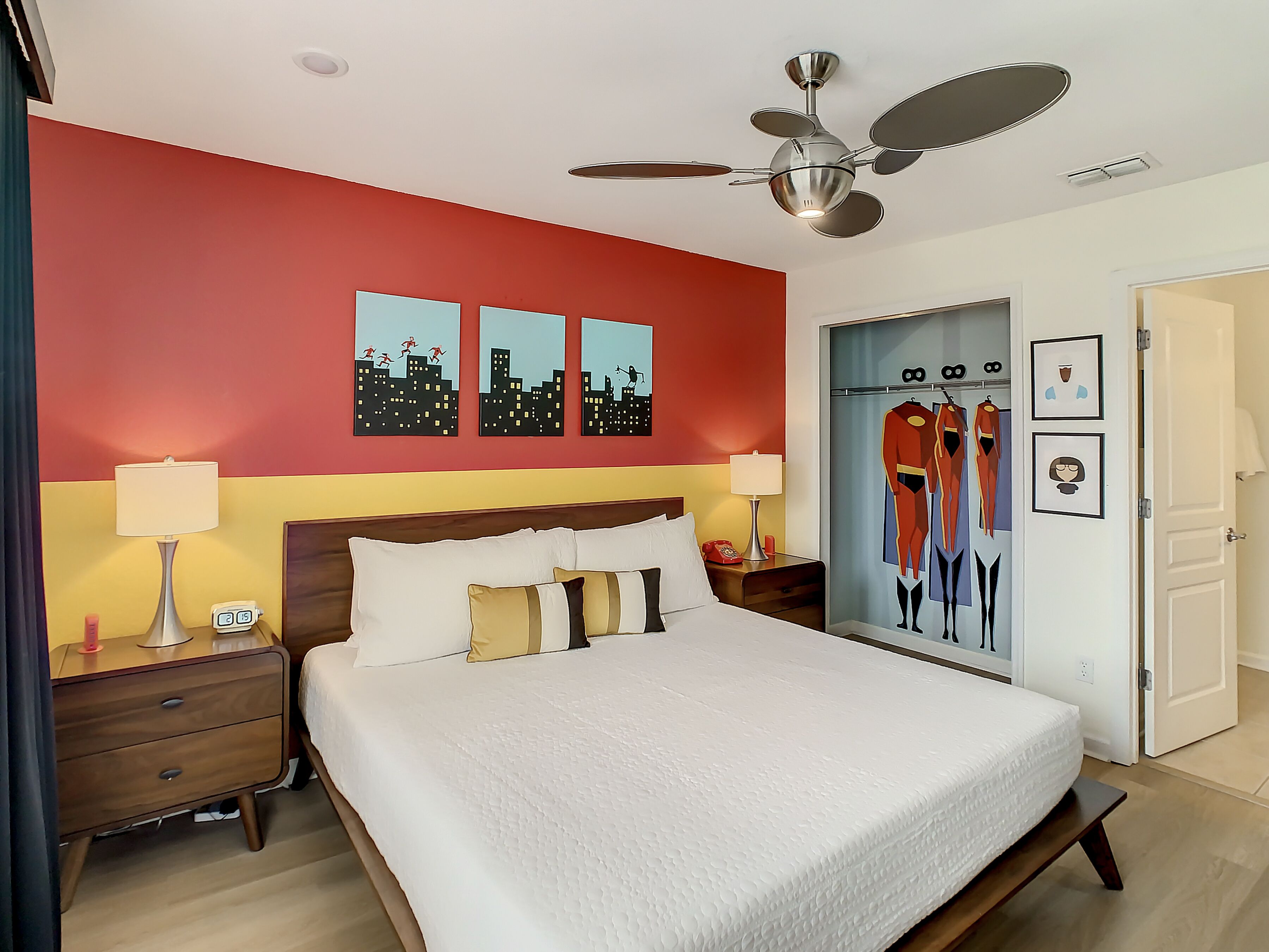 A hotel room with a large bed, a ceiling fan, artwork on the walls, and a door with a mirror.