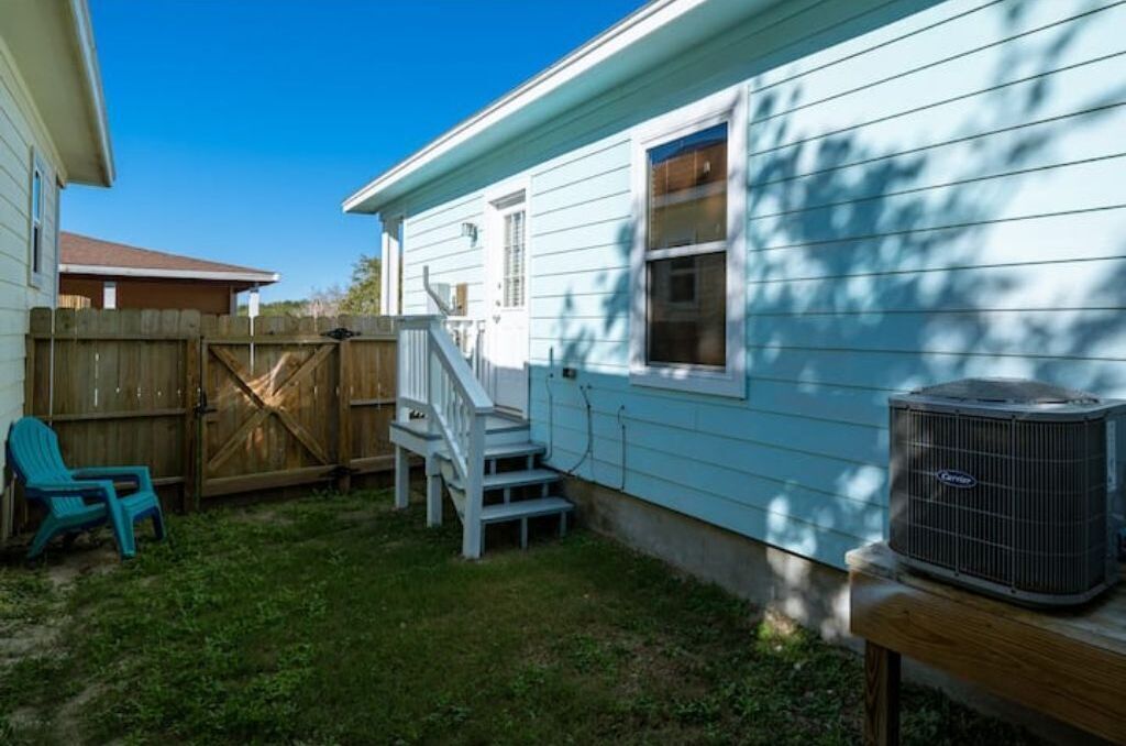 Una casa con terraza de madera, fachada azul y unidad de aire acondicionado.