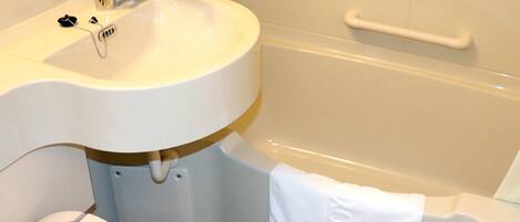 Un baño con lavamanos blanco, bañera y toalla blanca colgada en un perchero.