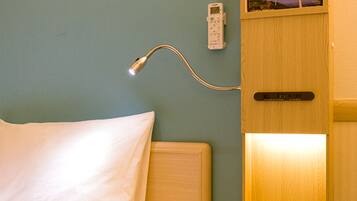 Une chambre d’hôtel comprenant un lit, une table de chevet, une commode, un téléphone fixé au mur et un panneau de commande.