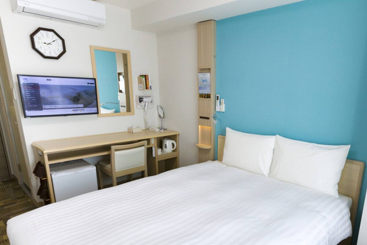 Een hotelkamer met een bed, een bureau, een stoel, een klok, een televisie en een spiegel.