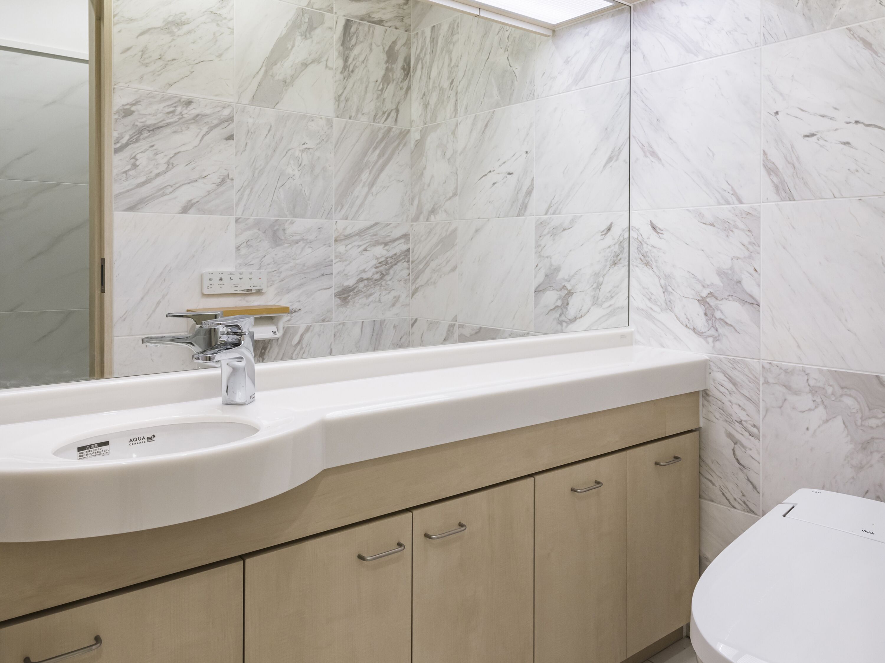 A bathroom with a white sink, marble tiles, and a toilet.