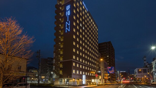A tall hotel with multiple floors and balconies, surrounded by urban buildings and a street with vehicles.