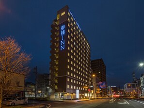 Un hotel alto con varios pisos y balcones, rodeado de edificios urbanos y una calle con vehículos.