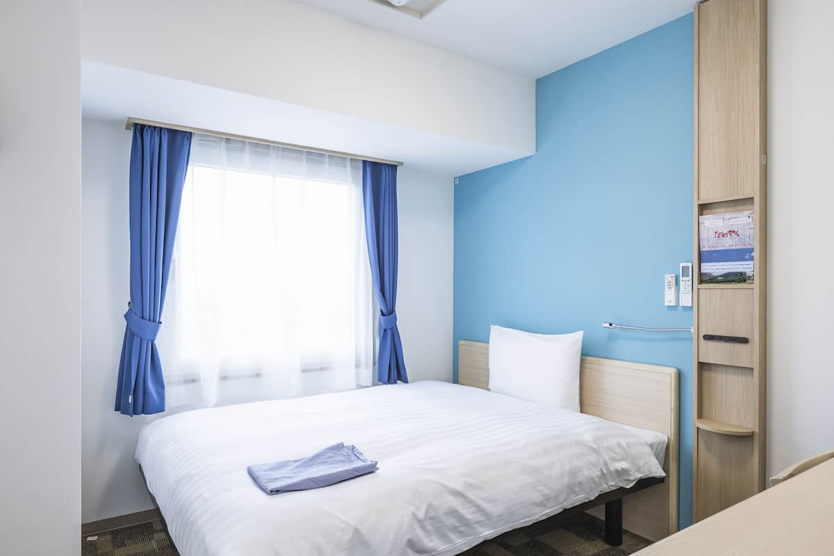 Een hotelkamer met een bed, een bureau, een kledingkast en een raam met gordijnen.