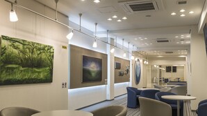A modern hotel lobby with round tables, blue and beige chairs, and artwork on the walls.
