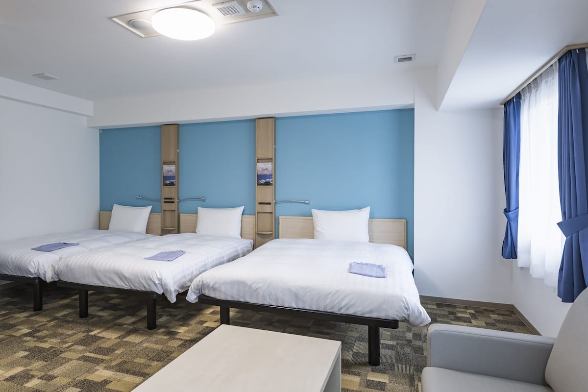 Een hotelkamer met twee éénpersoonsbedden, een klein tafeltje, een stoel en een raam met gordijnen.