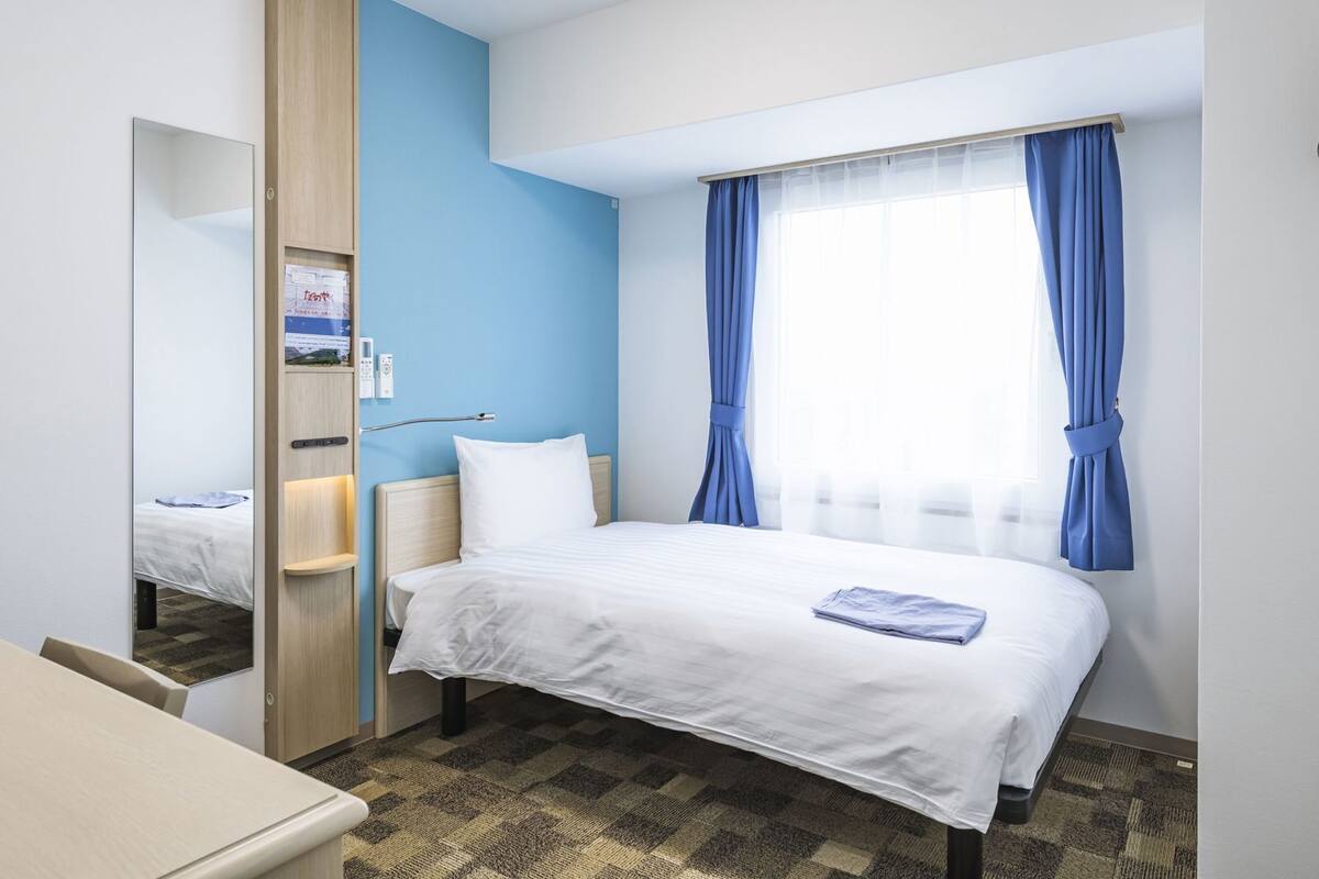 Een hotelkamer met een bed, een bureau, een spiegel en een raam met gordijnen.
