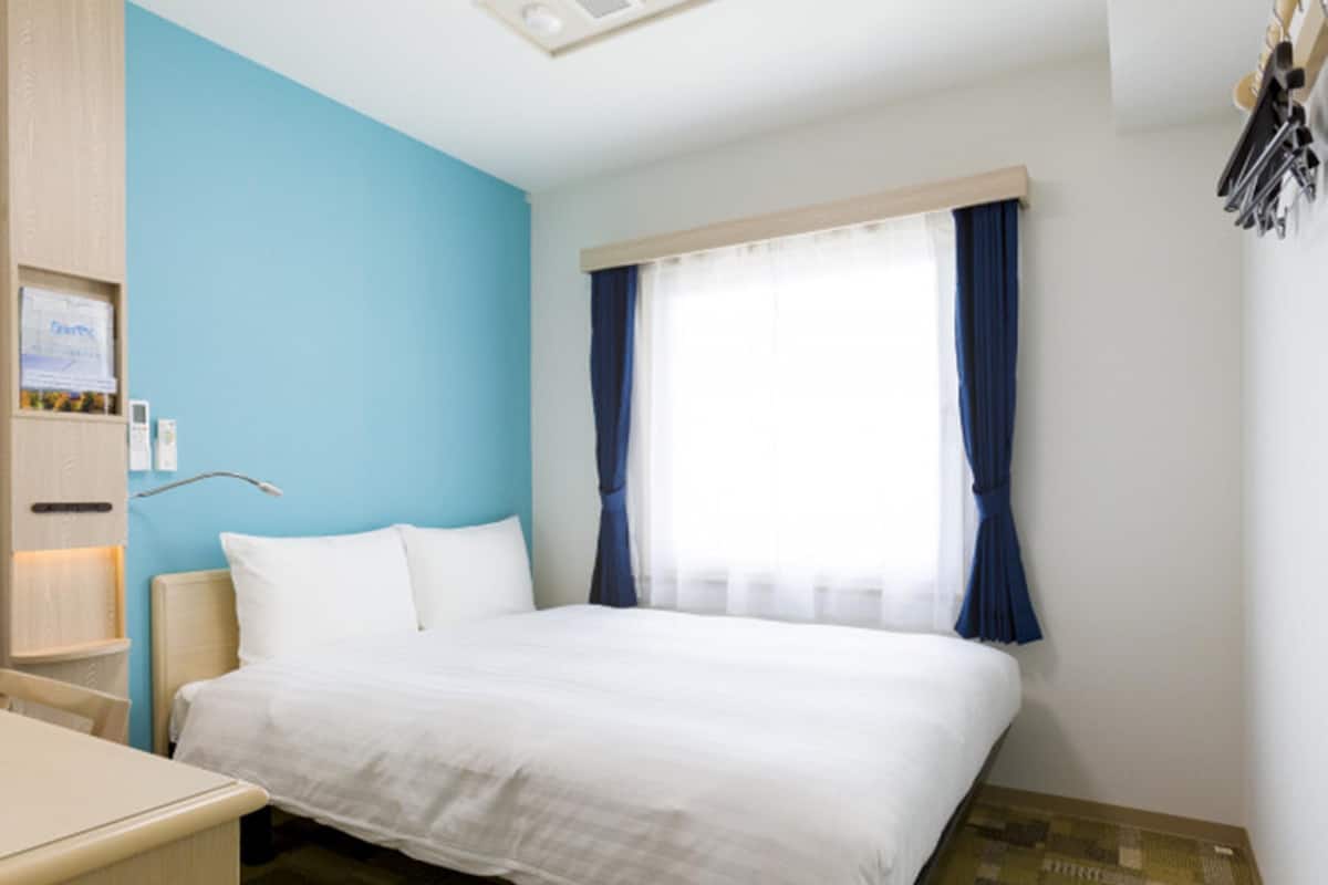 Een hotelkamer met een bed, een bureau, een nachtkastje en een raam met gordijnen.